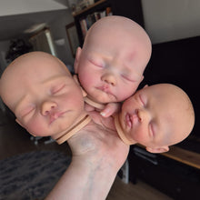 A person holding three realistic sleeping newborn baby doll heads with detailed skin textures and realistic skin tones, in a home setting.